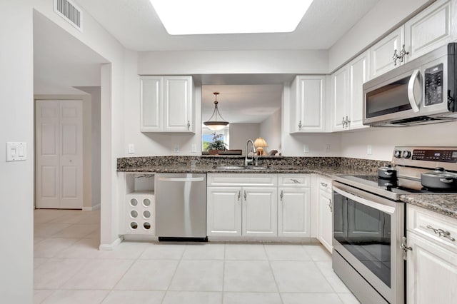 kitchen featuring light tile patterned floors, stainless steel appliances, white cabinetry, sink, and dark stone counters