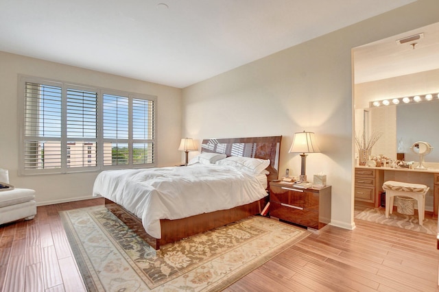 bedroom with light wood-style floors, baseboards, visible vents, and connected bathroom