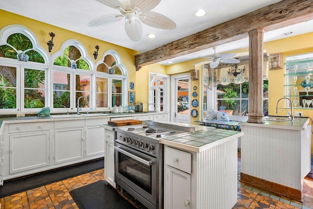 kitchen featuring white cabinets, beam ceiling, stainless steel range, and dark tile patterned flooring