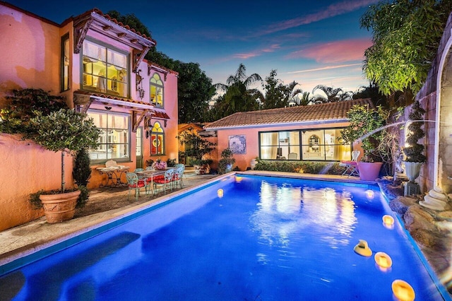 pool at dusk featuring a patio area and pool water feature