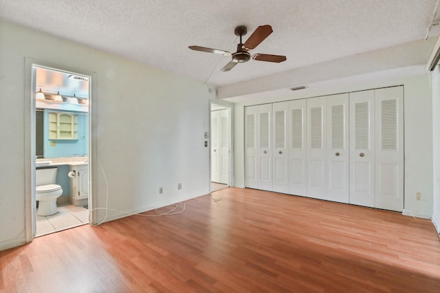 unfurnished bedroom featuring visible vents, a ceiling fan, light wood-style flooring, ensuite bathroom, and a textured ceiling