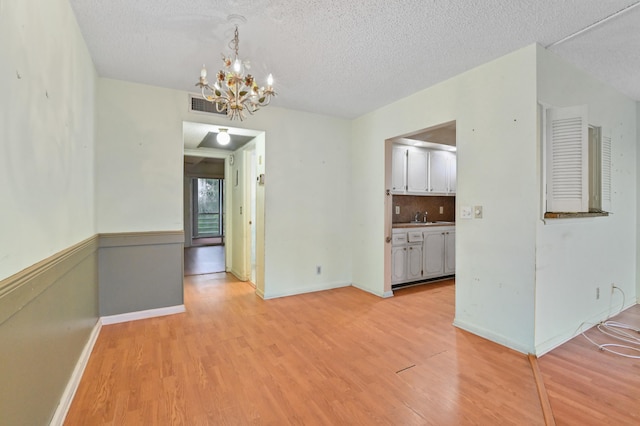 unfurnished dining area with light wood-type flooring, visible vents, a sink, and a notable chandelier