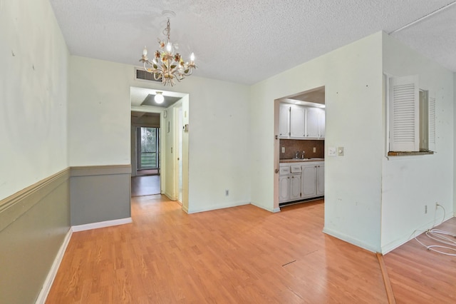 unfurnished dining area featuring a textured ceiling, a notable chandelier, visible vents, and light wood-type flooring
