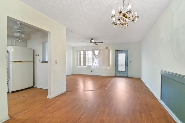 unfurnished living room with ceiling fan with notable chandelier, a textured ceiling, baseboards, and wood finished floors