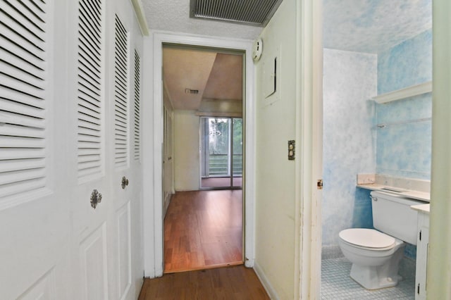 corridor featuring dark wood-style floors, a textured ceiling, visible vents, and baseboards