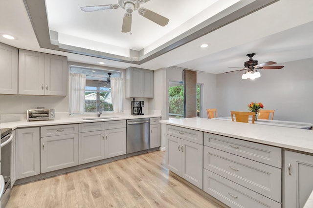 kitchen featuring light hardwood / wood-style floors, sink, gray cabinets, a tray ceiling, and appliances with stainless steel finishes