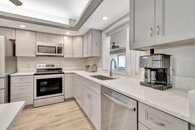 kitchen with light hardwood / wood-style floors, sink, appliances with stainless steel finishes, light stone countertops, and gray cabinets