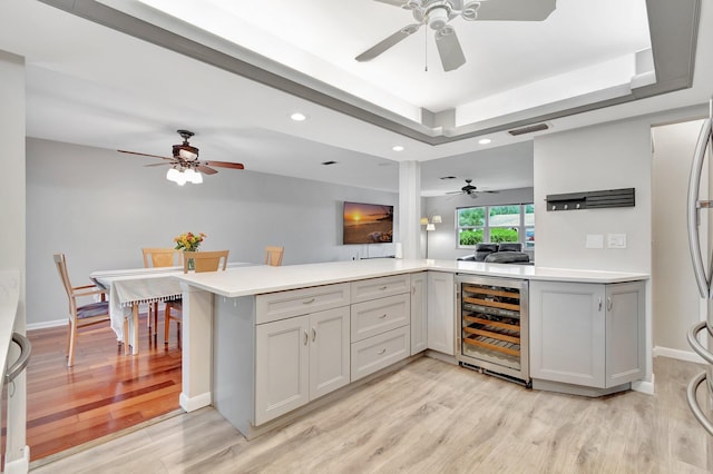 kitchen with kitchen peninsula, light hardwood / wood-style floors, a raised ceiling, and beverage cooler