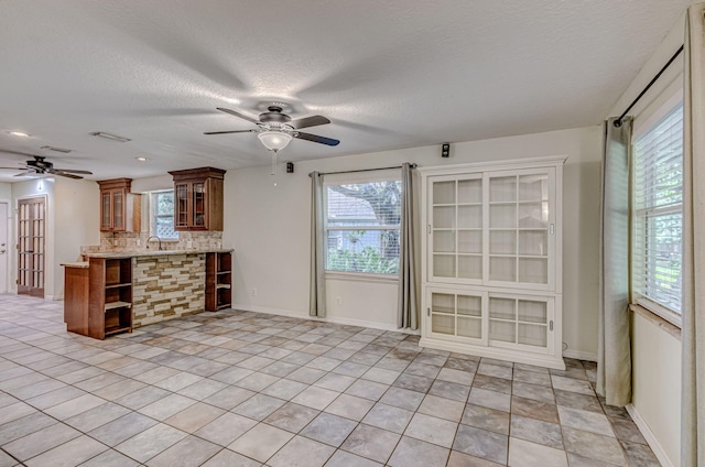 interior space featuring backsplash, sink, a textured ceiling, light tile patterned floors, and ceiling fan