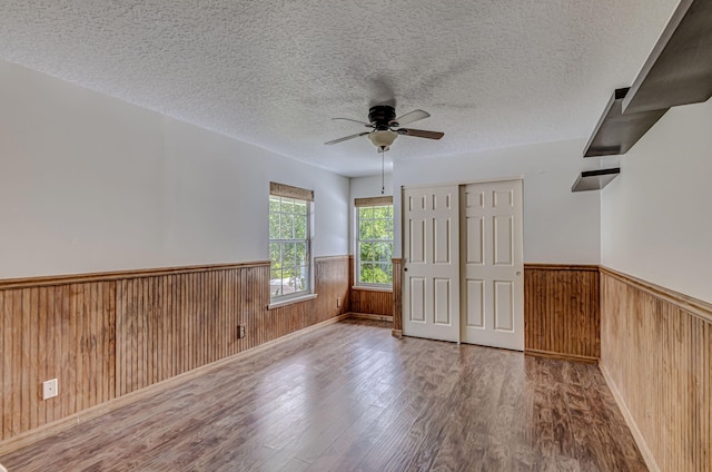 unfurnished room with a textured ceiling, wooden walls, ceiling fan, and hardwood / wood-style flooring