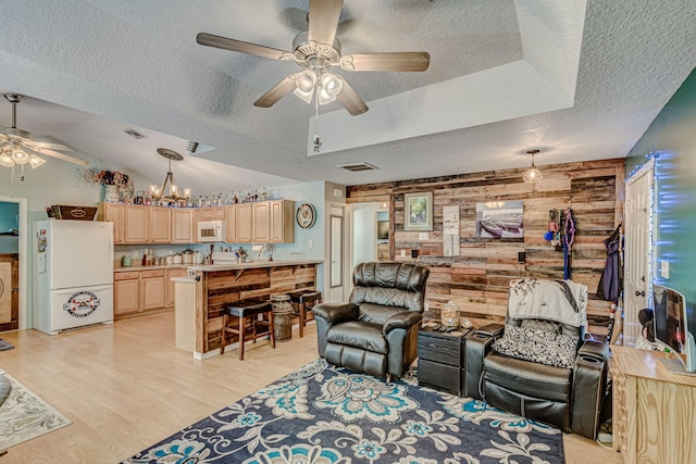 living room with wood walls, light hardwood / wood-style flooring, sink, a textured ceiling, and ceiling fan with notable chandelier