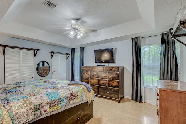 bedroom featuring a tray ceiling, light hardwood / wood-style floors, ceiling fan, and multiple windows