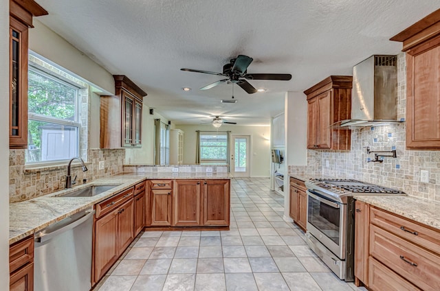 kitchen featuring ceiling fan, wall chimney exhaust hood, plenty of natural light, sink, and stainless steel appliances