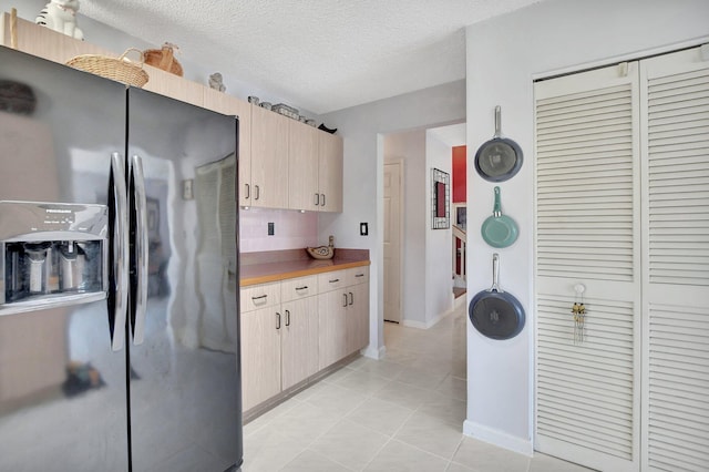 kitchen with stainless steel refrigerator with ice dispenser, a textured ceiling, light brown cabinets, and light tile patterned flooring