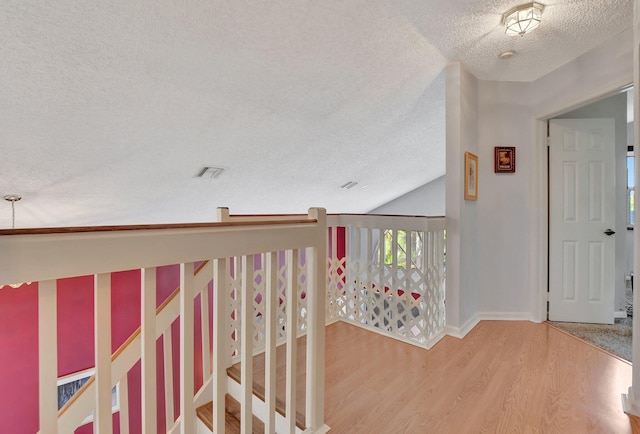 corridor with hardwood / wood-style floors, a textured ceiling, and vaulted ceiling