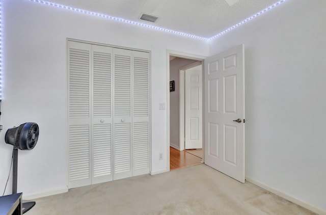 unfurnished bedroom with a textured ceiling, light colored carpet, and a closet