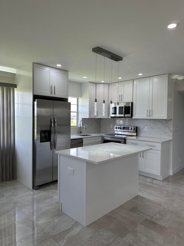 kitchen with hanging light fixtures, appliances with stainless steel finishes, a kitchen island, sink, and white cabinetry