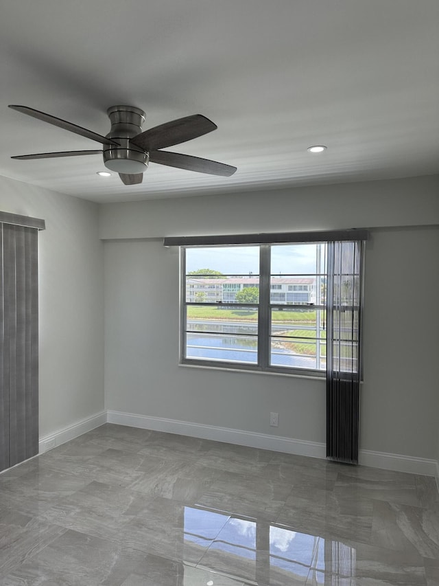 empty room featuring a water view, ceiling fan, baseboards, and recessed lighting