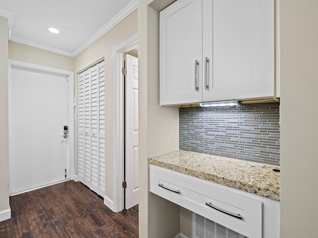 kitchen featuring dark hardwood / wood-style floors, light stone countertops, backsplash, ornamental molding, and white cabinetry