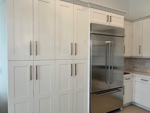 kitchen with decorative backsplash, light tile patterned floors, stainless steel built in refrigerator, and white cabinets