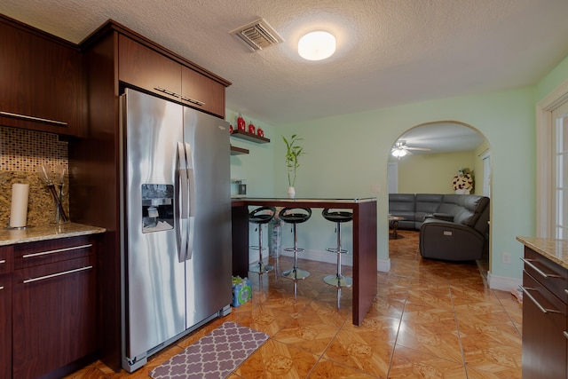 kitchen with backsplash, stainless steel fridge, a textured ceiling, and light stone counters