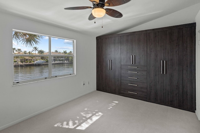 unfurnished bedroom with ceiling fan, light colored carpet, a closet, vaulted ceiling, and a water view