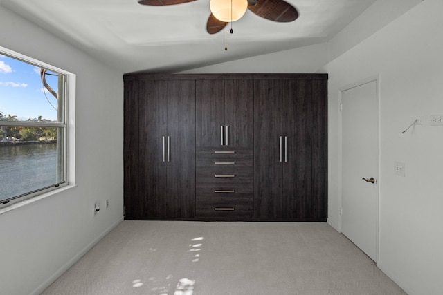 unfurnished bedroom featuring ceiling fan, light carpet, vaulted ceiling, and a water view