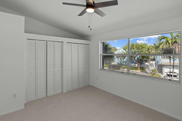 unfurnished bedroom featuring ceiling fan, carpet floors, lofted ceiling, and two closets