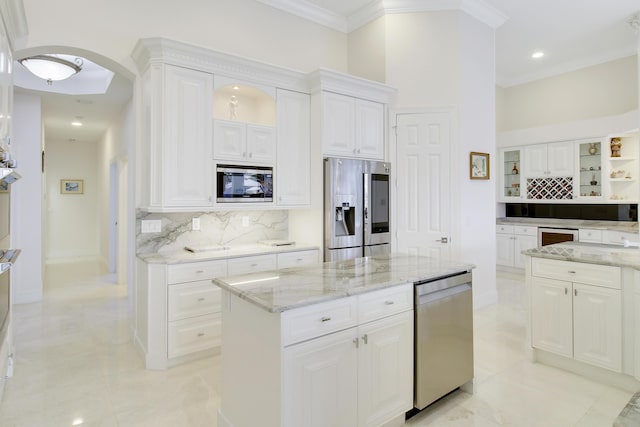 kitchen with light stone countertops, a center island, stainless steel appliances, backsplash, and white cabinets