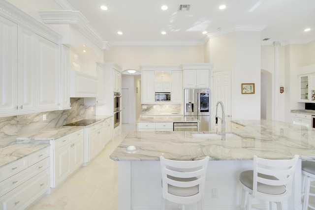 kitchen featuring appliances with stainless steel finishes, white cabinetry, a breakfast bar area, and a large island with sink