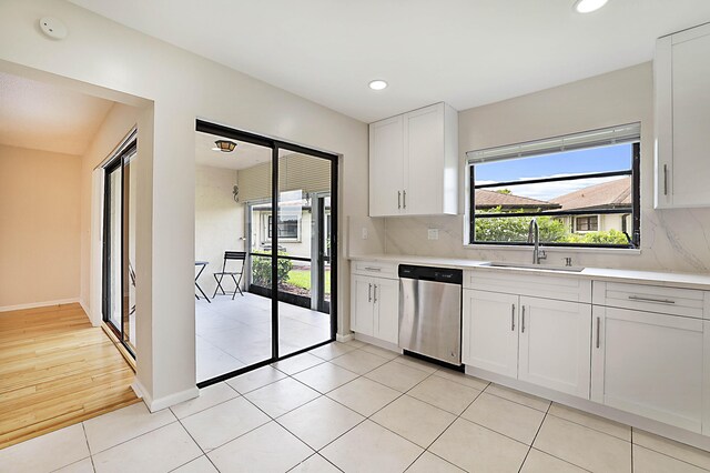 kitchen with light tile patterned flooring, sink, white cabinetry, stainless steel dishwasher, and backsplash