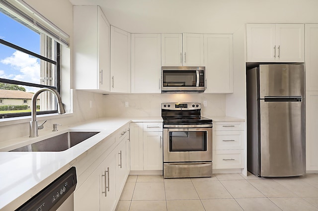 kitchen with stainless steel appliances, sink, light tile patterned floors, and white cabinets