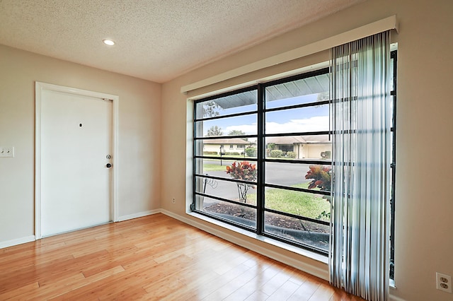 doorway to outside with plenty of natural light, a textured ceiling, and light wood-type flooring