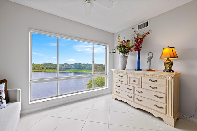 bedroom with light tile patterned flooring, ceiling fan, a water view, and a textured ceiling