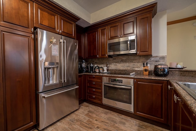 kitchen featuring decorative backsplash, light hardwood / wood-style floors, dark stone counters, and appliances with stainless steel finishes