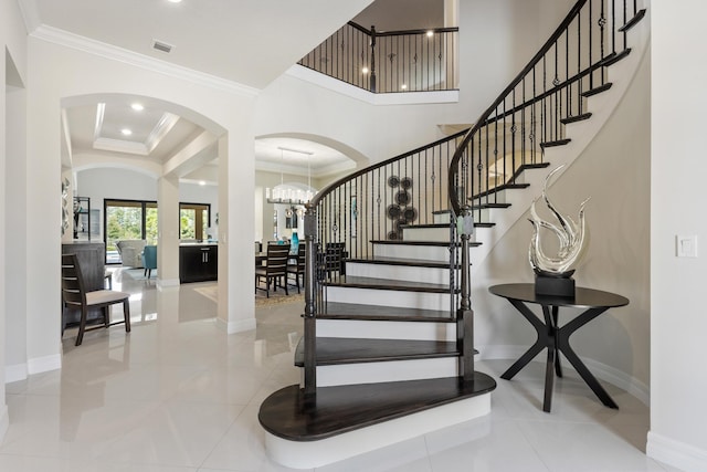 staircase featuring a tray ceiling, tile patterned floors, a chandelier, and ornamental molding