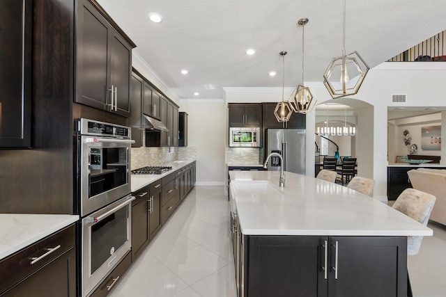 kitchen with backsplash, a breakfast bar, stainless steel appliances, hanging light fixtures, and an island with sink