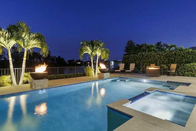 pool at night featuring an in ground hot tub, a patio, and a fire pit