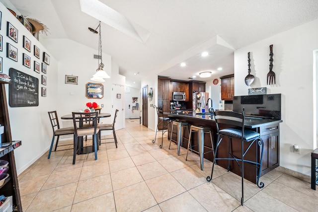 kitchen with vaulted ceiling with skylight, stainless steel appliances, light tile patterned floors, kitchen peninsula, and a breakfast bar