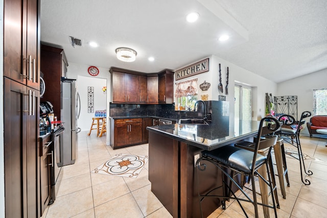 kitchen with decorative backsplash, stainless steel refrigerator, a kitchen bar, light tile patterned floors, and sink