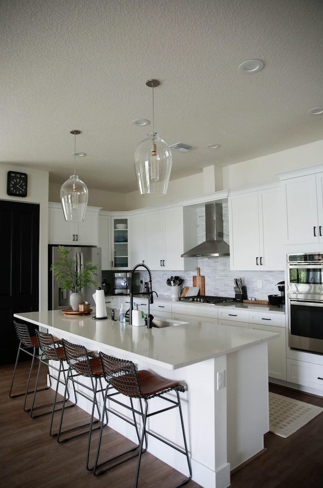 kitchen featuring stainless steel appliances, a spacious island, dark hardwood / wood-style floors, wall chimney range hood, and white cabinets