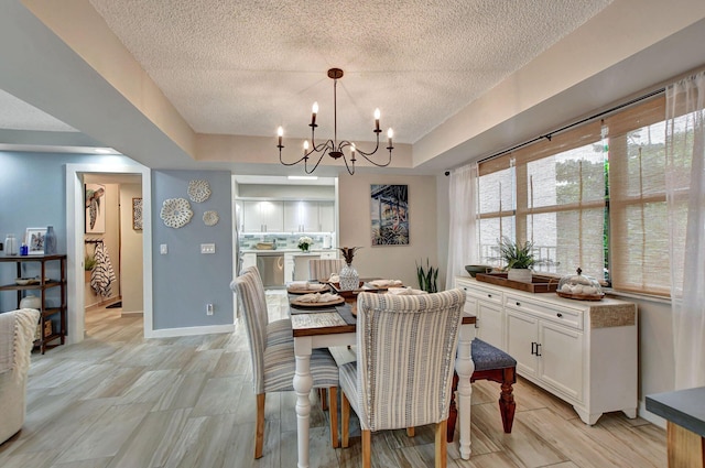 dining space featuring a textured ceiling, light wood-type flooring, a tray ceiling, and a notable chandelier