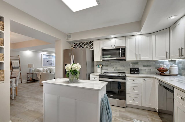 kitchen featuring white cabinets, stainless steel appliances, backsplash, and light stone countertops