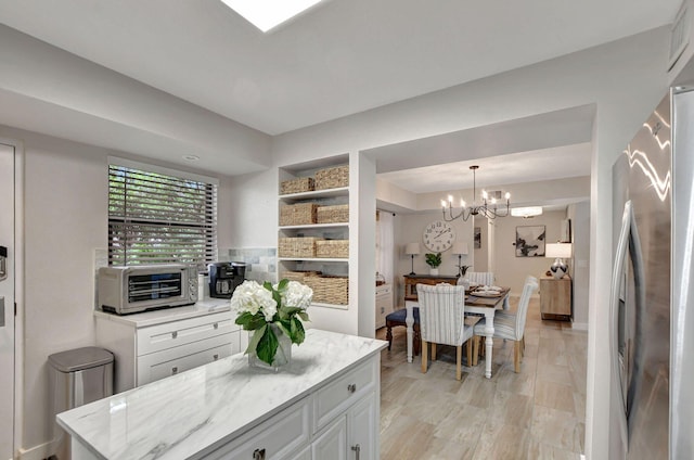 kitchen with a chandelier, white cabinetry, hanging light fixtures, stainless steel refrigerator, and light stone countertops