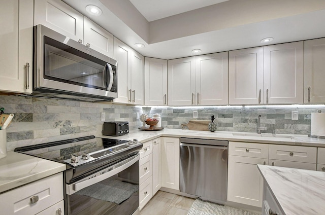 kitchen featuring decorative backsplash, light stone counters, white cabinets, stainless steel appliances, and sink