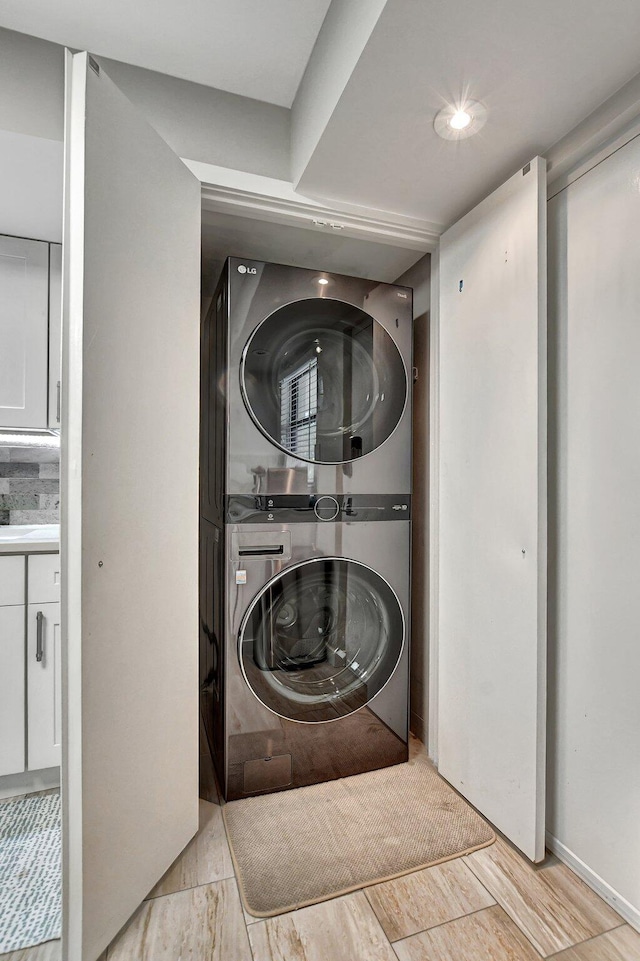 laundry area with light hardwood / wood-style floors and stacked washer / drying machine