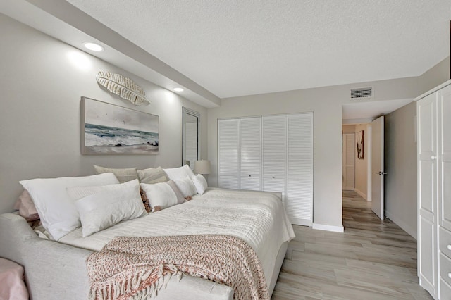 bedroom featuring a textured ceiling, light hardwood / wood-style floors, and multiple closets