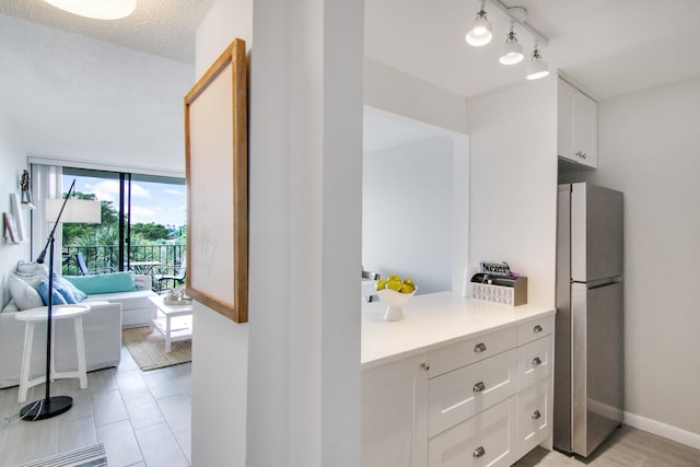 kitchen featuring a textured ceiling, stainless steel refrigerator, and white cabinetry