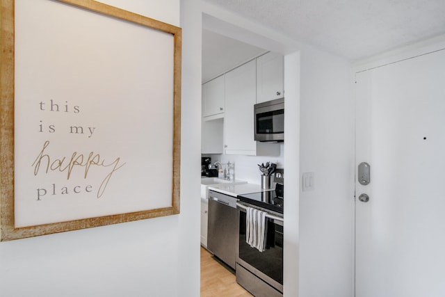 kitchen featuring stainless steel appliances, light hardwood / wood-style floors, white cabinetry, sink, and a textured ceiling