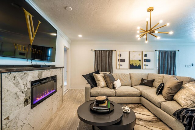 living room with crown molding, light wood-type flooring, a fireplace, a textured ceiling, and a notable chandelier